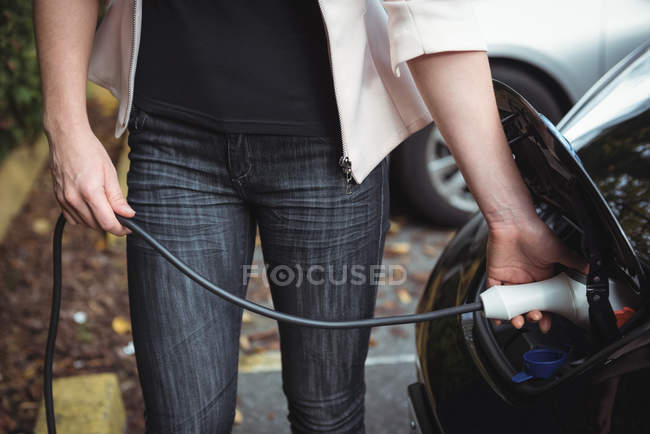 Seção média de mulher cobrando carro elétrico na rua — Fotografia de Stock