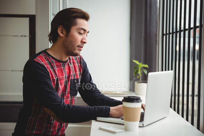 Homem usando laptop enquanto toma café na cafeteria — Fotografia de Stock