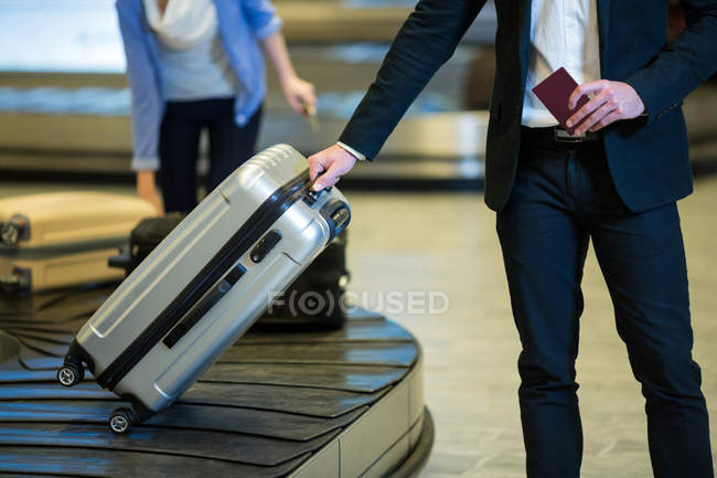 Mid section of businessman picking his luggage from baggage claim area at airport terminal — Stock Photo