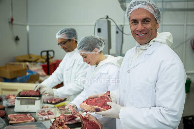 Ritratto di macellaio che sorride mentre tiene la carne in fabbrica — Foto stock