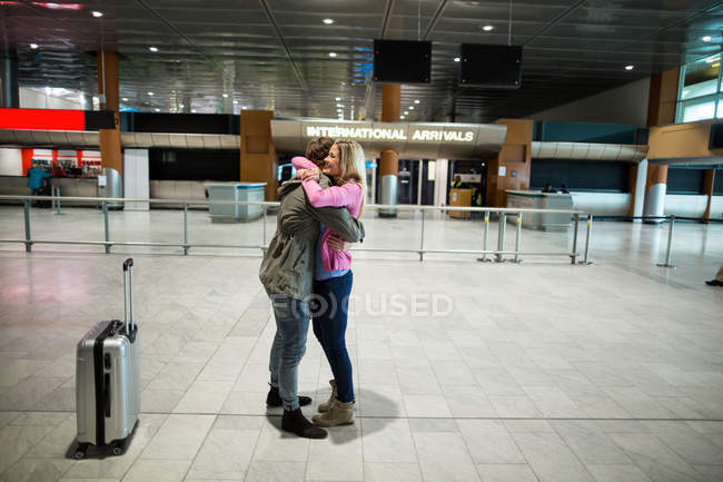 Pareja alegre abrazándose en la sala de espera en la terminal del aeropuerto - foto de stock