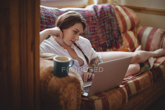 Красива жінка лежить на дивані і використовує ноутбук у вітальні вдома — стокове фото