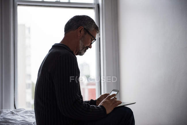 Homem usando tablet digital e telefone celular na sala de estar em casa — Fotografia de Stock