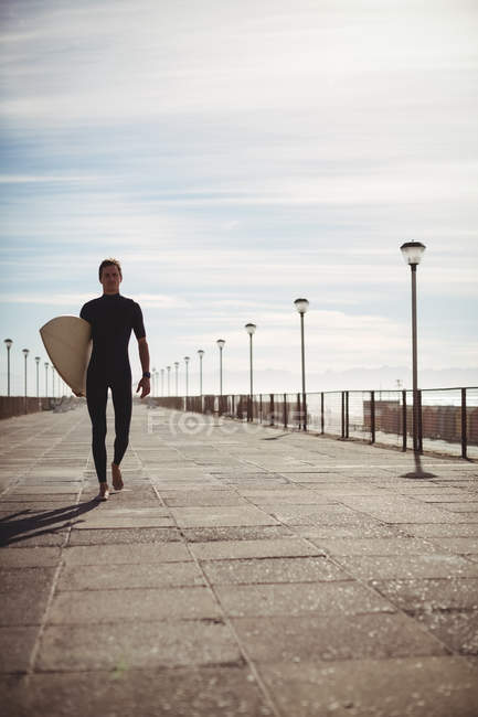 Surfista caminando con tabla de surf en el muelle en la playa - foto de stock