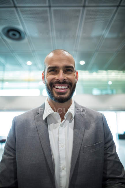 Улыбающийся бизнесмен, стоящий в зоне ожидания терминала аэропорта — стоковое фото