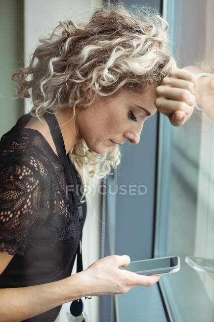 Расстроенная деловая женщина с помощью мобильного телефона в офисе — стоковое фото