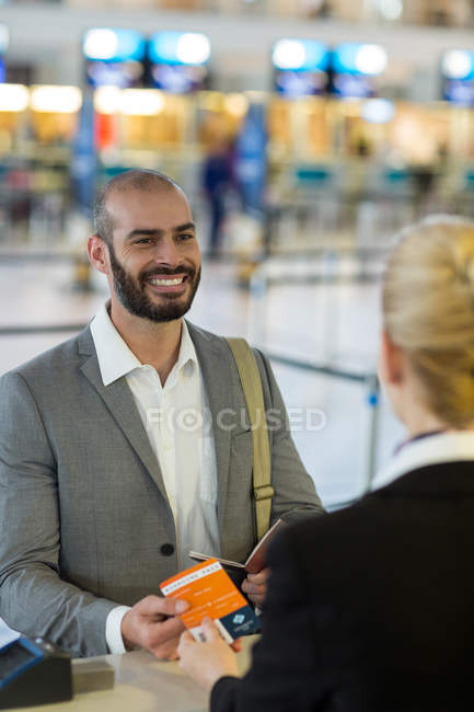 Atendedor de check-in da companhia aérea entrega cartão de embarque para pendulares no balcão no terminal do aeroporto — Fotografia de Stock