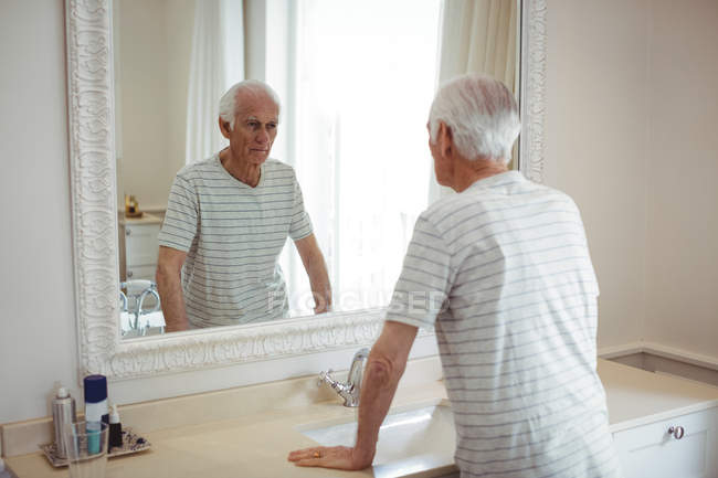 Hombre mayor mirando el espejo en el baño - foto de stock