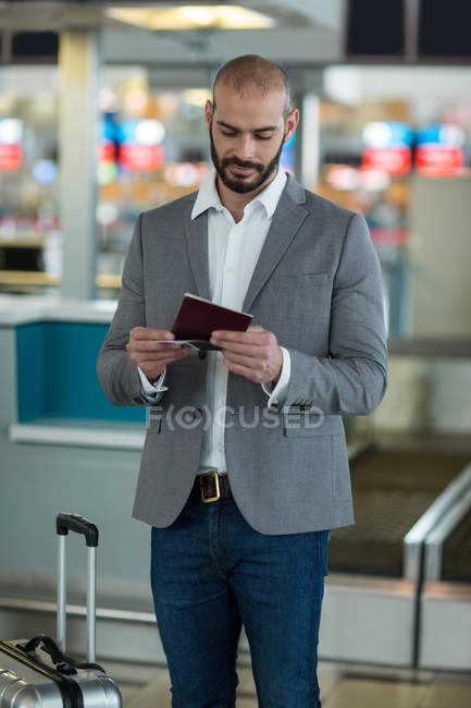 Businessman with luggage checking his boarding pass at airport terminal — Stock Photo
