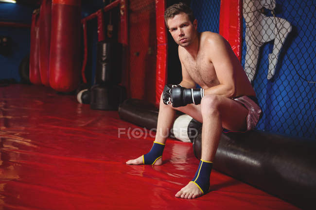 Male boxer sitting on punching bag in fitness studio — Stock Photo