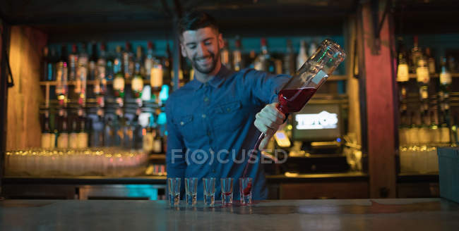 Cantinero vertiendo bebida alcohólica en vasos de chupito en el bar - foto de stock