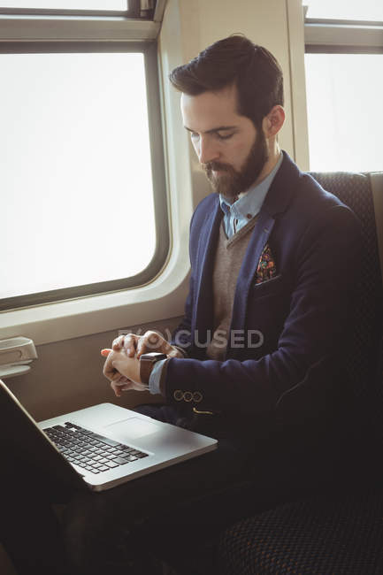 Homme d'affaires vérifier le temps tout en utilisant un ordinateur portable dans le train — Photo de stock