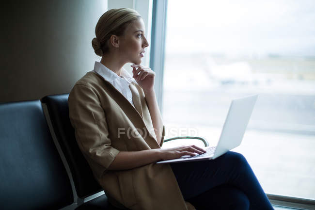 Nachdenkliche Frau benutzt Laptop im Wartebereich am Flughafen-Terminal — Stockfoto