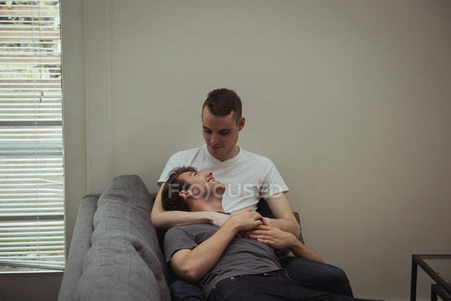 Romantic gay couple embracing on sofa at home — Stock Photo