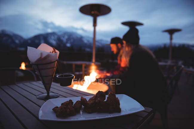 Pareja sentada junto al fuego contra el cielo al atardecer durante el invierno - foto de stock