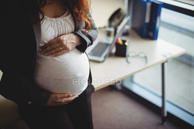 Schwangere Geschäftsfrau berührt Bauch im Büro — Stockfoto