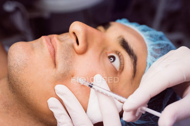 Человек получает инъекции ботокса на лице в клинике — стоковое фото