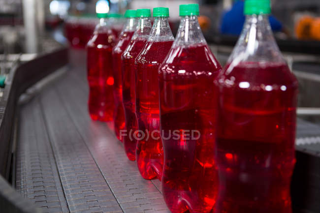 Llenado botellas de jugo rojo en la línea de producción en fábrica - foto de stock