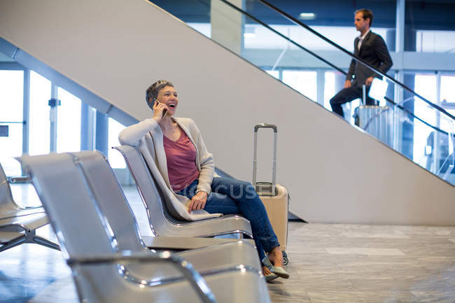 Mulher sorridente conversando no telefone celular na área de espera no terminal do aeroporto — Fotografia de Stock