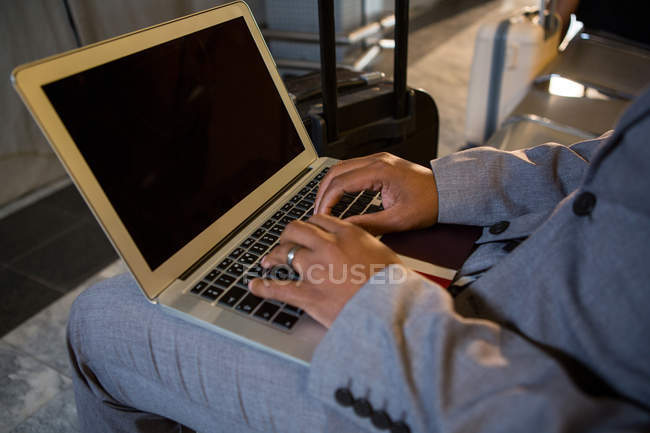 Homem usando laptop enquanto sentado na área de espera no terminal do aeroporto — Fotografia de Stock