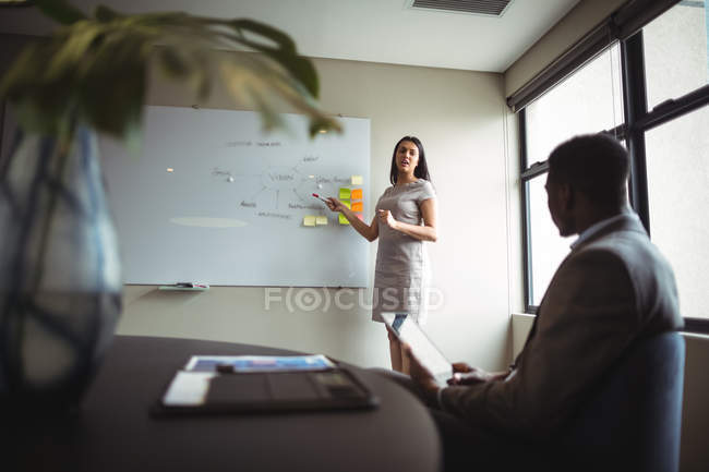 Empresaria discutiendo en pizarra blanca con un colega en la oficina - foto de stock