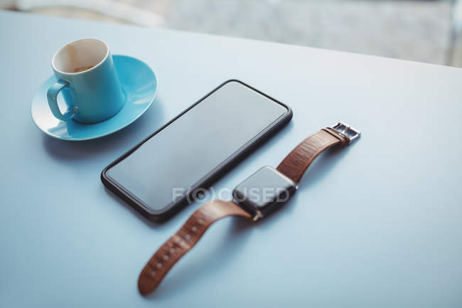 Wristwatch, mobile phone and cup of coffee at counter in cafeteria — Stock Photo