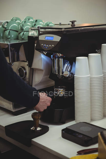 Mano del hombre sosteniendo portafilter bajo la máquina de café en la cafetería - foto de stock