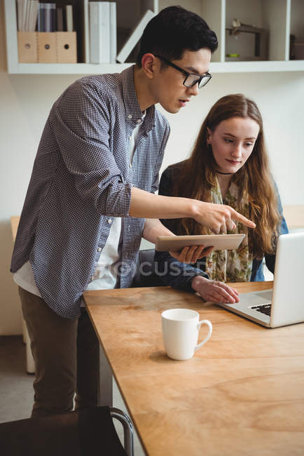 Dirigeants d'entreprise discutant sur ordinateur portable et tablette numérique au bureau — Photo de stock