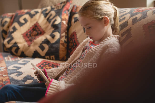 Дівчина сидить на дивані і використовує цифровий планшет у вітальні вдома — стокове фото