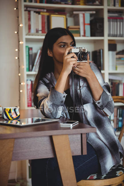 Mujer tomando fotos en la cámara vintage en la sala de estar en casa - foto de stock