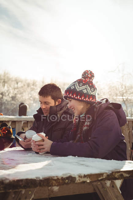 Feliz casal esquiador usando telefone celular e tablet digital à mesa na estância de esqui — Fotografia de Stock