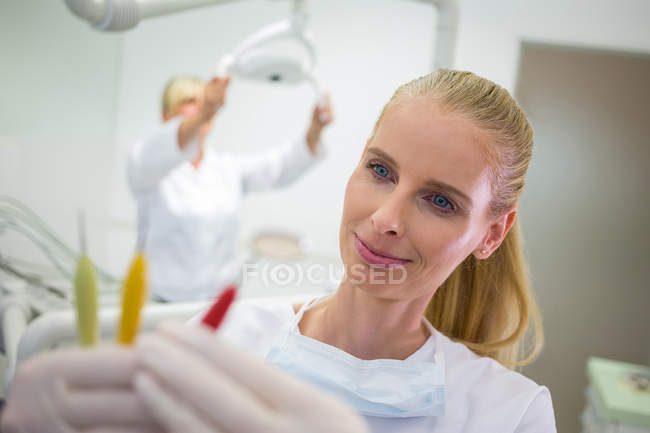 Dentiste souriant regardant les outils dentaires dans la clinique — Photo de stock
