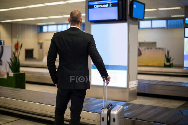 Vista posteriore dell'uomo d'affari in piedi con i bagagli in sala d'attesa in aeroporto — Foto stock