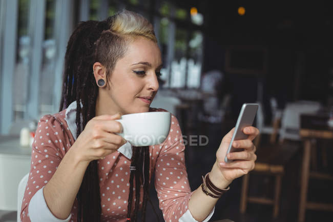 Woman using mobile phone while having coffee in cafe — Stock Photo