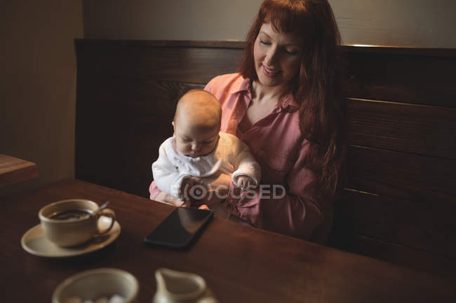 Mãe segurando bebê bonito nos braços na mesa de café — Fotografia de Stock