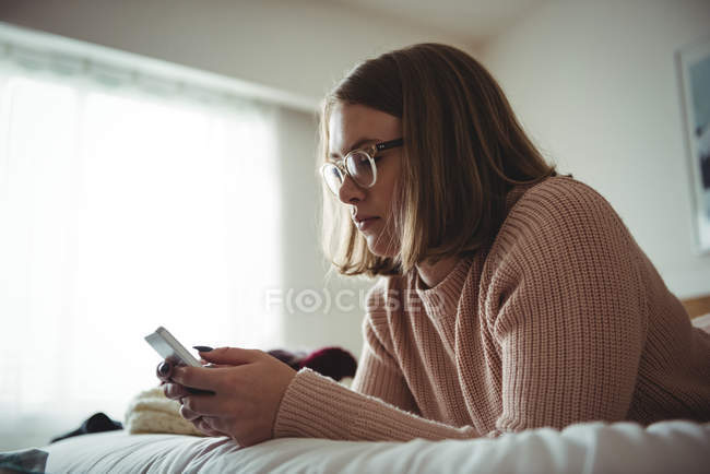 Жінка лежить на ліжку, використовуючи мобільний телефон у спальні вдома — стокове фото