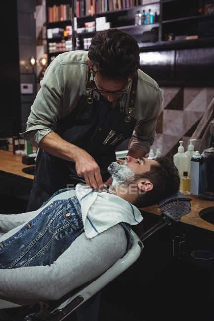 Mann rasiert sich Bart bei Friseur mit Rasiermesser im Friseurladen — Stockfoto
