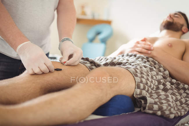 Fisioterapeuta realizando agujas electro-secas en la rodilla del paciente en clínica - foto de stock
