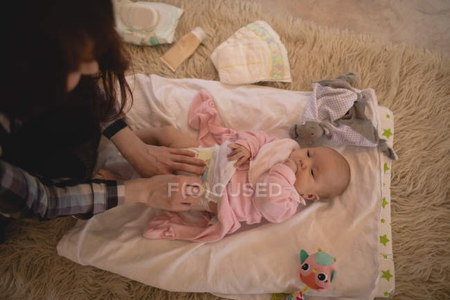 Mãe mudando fralda de bebê na sala de estar em casa — Fotografia de Stock