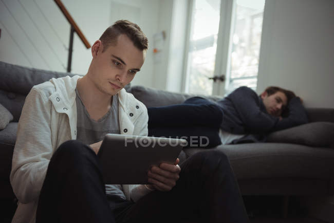 Людина використовує цифровий планшет, а його друг спить у фоновому режимі на дивані — стокове фото