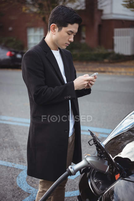 Людина використовує мобільний телефон під час заряджання автомобіля на зарядній станції електромобіля — стокове фото