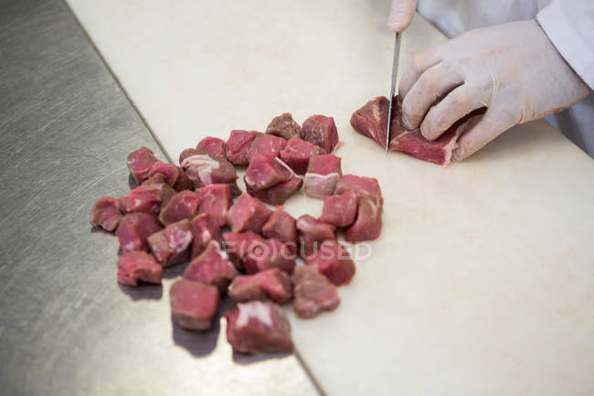 Nahaufnahme eines Metzgers, der in einer Fleischfabrik Fleisch in kleine Stücke schneidet — Stockfoto