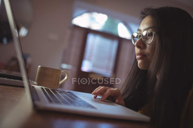 Femme utilisant un ordinateur portable sur la table dans le salon à la maison — Photo de stock