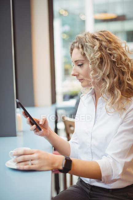 Mujer de negocios reflexivo uso de teléfono inteligente en el mostrador en la cafetería - foto de stock