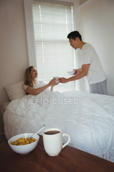 Мужчина подает завтрак женщине в спальне дома — стоковое фото