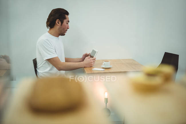 Hombre usando tableta digital en la cafetería con una taza de café en la mesa - foto de stock