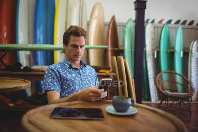 Человек, сидящий в магазине серфинга и пользующийся мобильным телефоном — стоковое фото