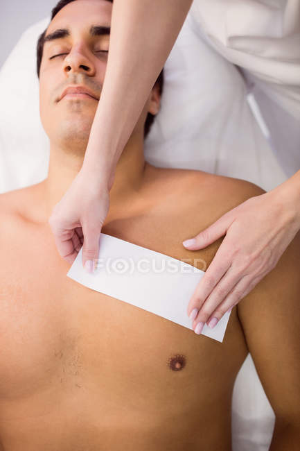 Homem recebendo depilação no peito com tira de cera na clínica — Fotografia de Stock