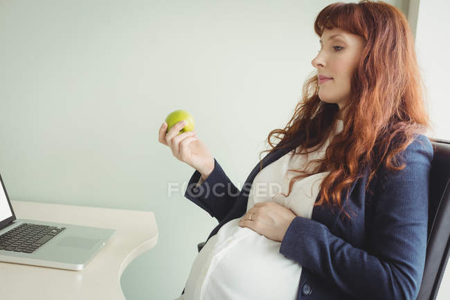 Pregnant businesswoman holding apple in office — Stock Photo