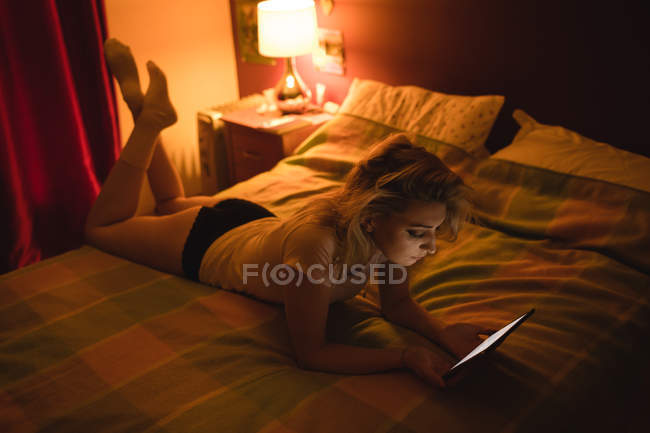 Femme couchée et utilisant une tablette numérique sur le lit dans la chambre — Photo de stock